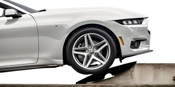 Side view of a car driving smoothly over a concrete curb using a driveway curb ramp, demonstrating effective curb transition.