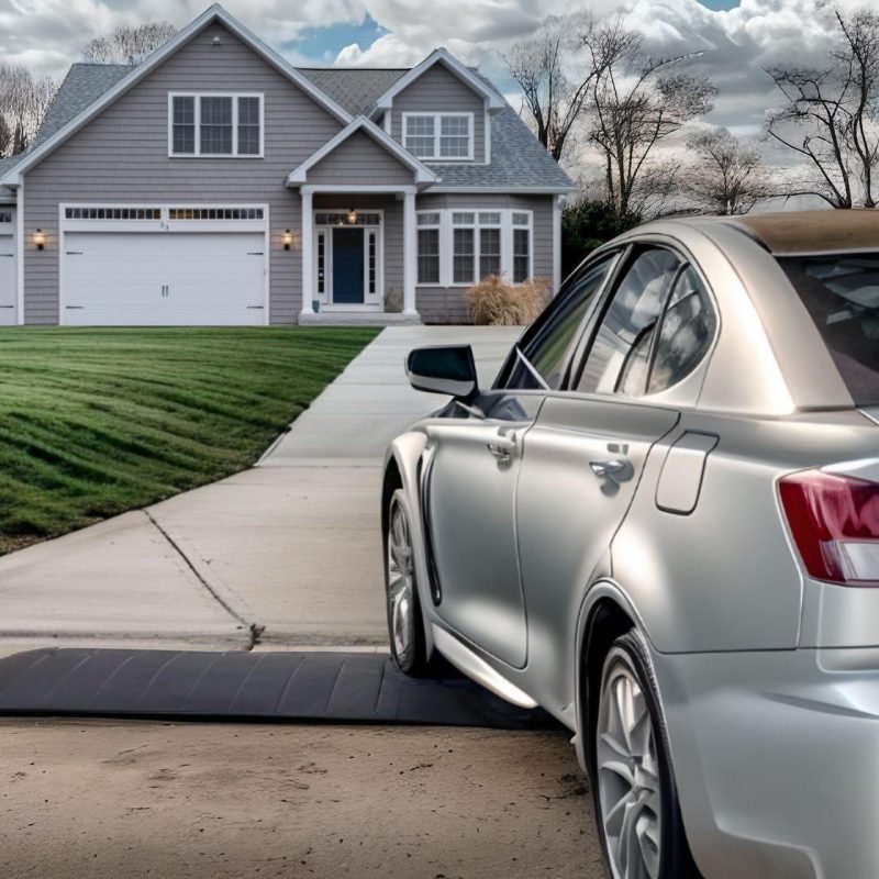 Silver car driving over a smooth driveway curb ramp for low car clearance in front of a suburban home.