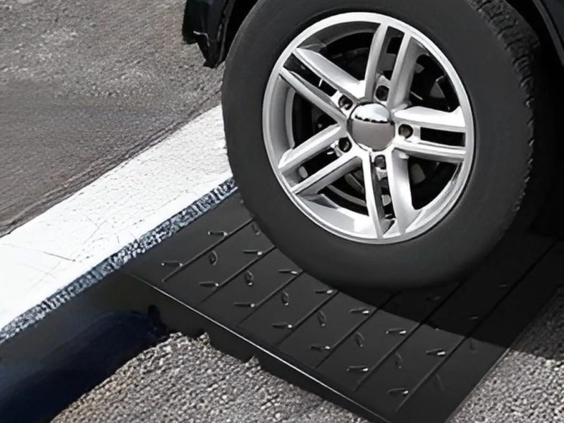 Close-up of a vehicle tire using a heavy-duty driveway ramp to safely cross a steep curb