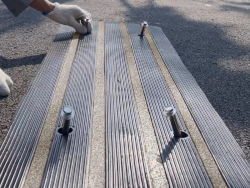 Close-up of concrete anchors being inserted into predrilled holes in a driveway ramp to provide secure, stable installation.