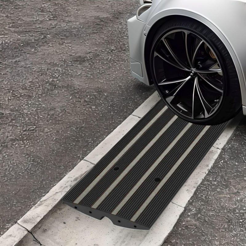 Close-up of a car wheel crossing a street gutter using a black curb ramp, preventing scraping and ensuring smooth driveway access.