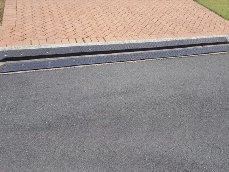 DIY curb ramp installed on a brick driveway entry with a concrete curb for improved vehicle accessibility.