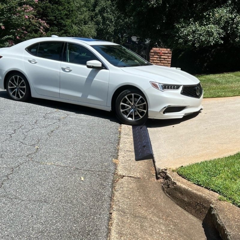 A white low-clearance car using a driveway ramp to smoothly navigate a steep driveway curb without scraping.