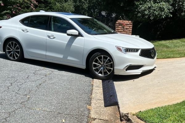 A white low-clearance car using a driveway ramp to smoothly navigate a steep driveway curb without scraping.