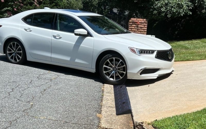 A white low-clearance car using a driveway ramp to smoothly navigate a steep driveway curb without scraping.