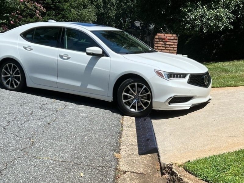 A white low-clearance car using a driveway ramp to smoothly navigate a steep driveway curb without scraping.