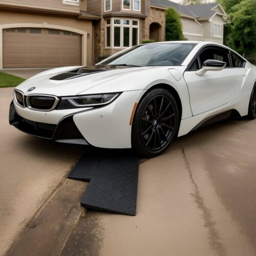 Low BMW i8 climbing over a driveway gutter threshold using paired rubber ramps to prevent front-end scraping.