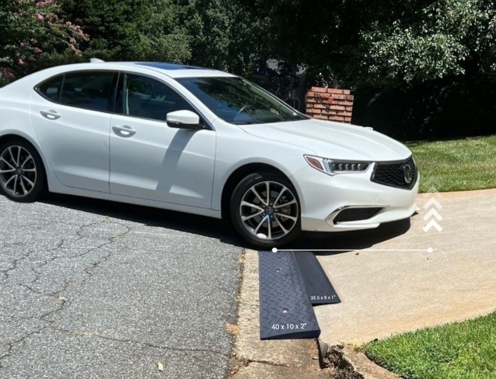 Low clearance vehicle smoothly driving over a steep driveway curb ramp, preventing car scraping and damage to the undercarriage.