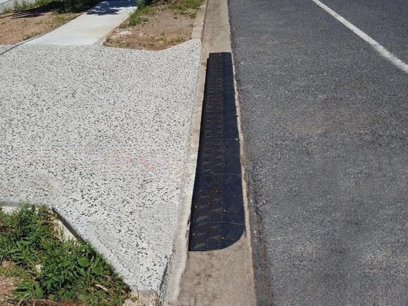 Mountable rubber curb ramp installed along a driveway edge, ensuring smooth vehicle transitions over a curb lip.