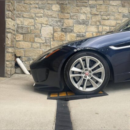 Low-clearance car scraping over a steep driveway drain without enough clearance support.
