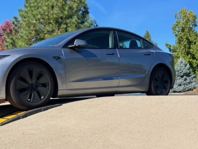 Low-clearance electric car driving up a steep driveway using a curb ramp to prevent underbody scraping.