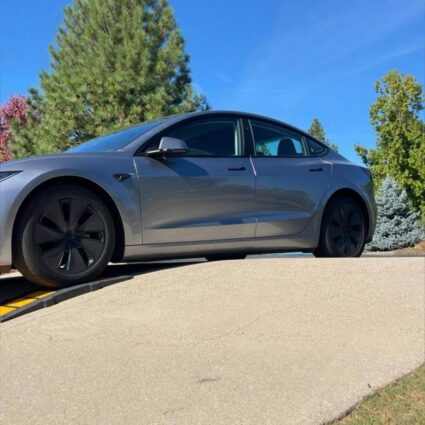 Low-clearance car entering a steep driveway using a curb ramp to prevent scraping at the driveway transition.