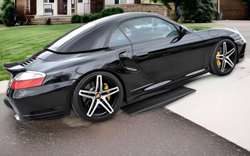 Black sports car driving over low clearance driveway curb ramp, designed to prevent scraping on steep driveways.