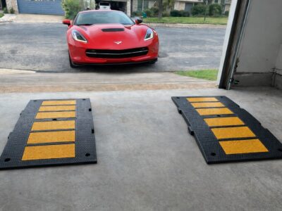 Low sports car approaching a steep garage driveway with rubber ramps aligned under the tires to prevent scraping.