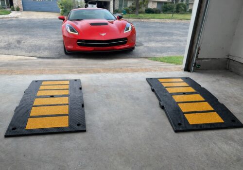 Low sports car approaching a steep garage driveway with rubber ramps aligned under the tires to prevent scraping.