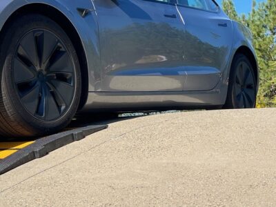 Tesla with low ground clearance climbing a steep driveway using a rubber driveway ramp to avoid scraping.