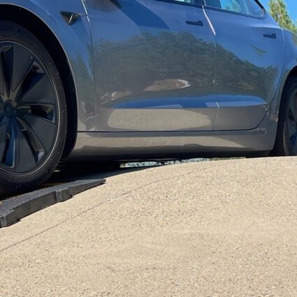 Tesla with low ground clearance climbing a steep driveway using a rubber driveway ramp to avoid scraping.