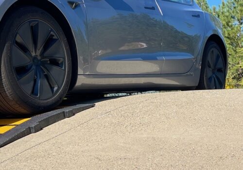 Tesla with low ground clearance climbing a steep driveway using a rubber driveway ramp to avoid scraping.