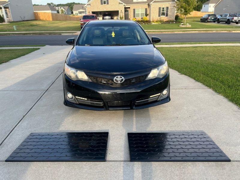 A black car facing the driveway with two heavy-duty curb ramps in place, ready for use to ensure smooth entry without scraping