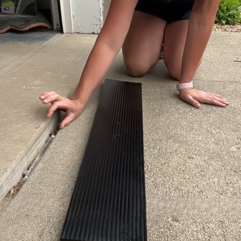 A person positioning a long rubber ramp at the threshold of a garage entryway, demonstrating easy installation.