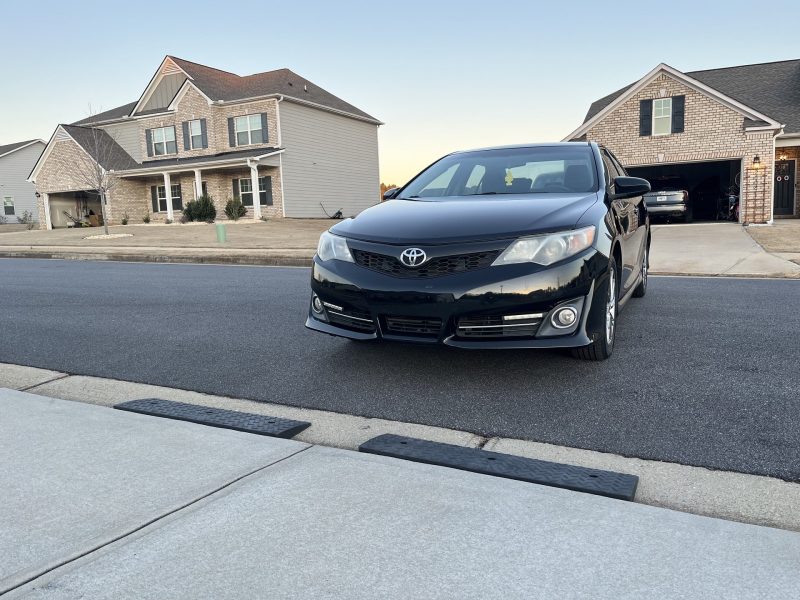 Black car approaching a driveway ramp designed for low clearance vehicles and steep driveway lips.