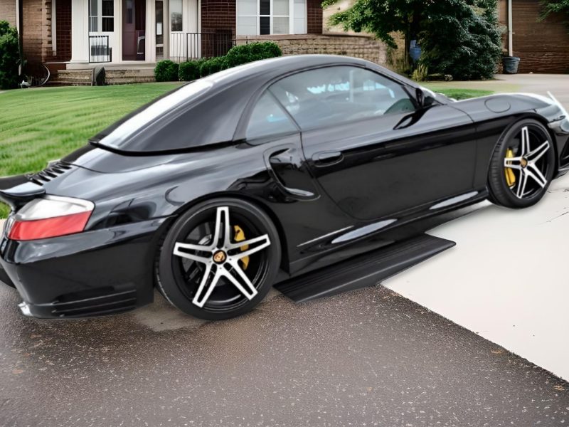 Low sports car entering a steep driveway with a clearance ramp to prevent scraping.