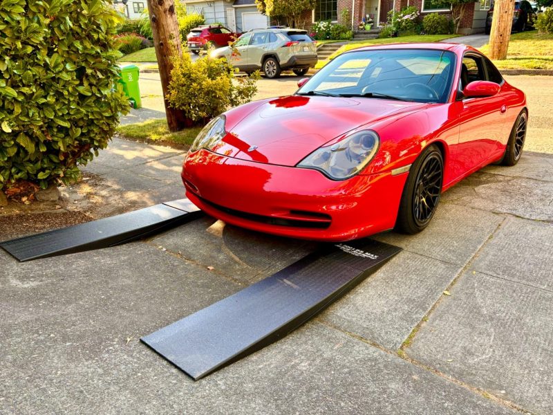 Red low-clearance sports car using driveway entry ramps to prevent scraping on a steep incline.