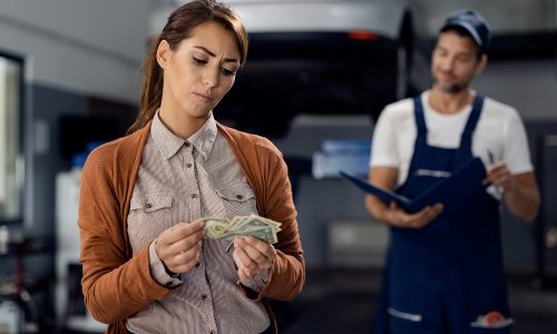 Displeased woman counting money to pay a bill for car repair at workshop.