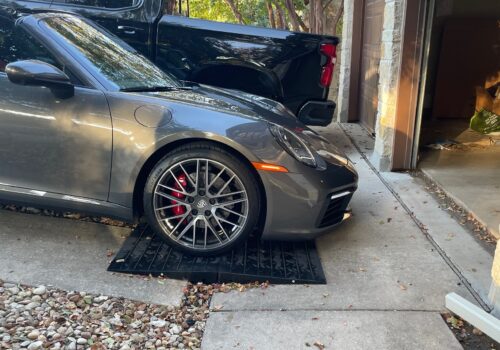 Low sports car using modular rubber ramps to prevent front lip scraping on a steep driveway transition.