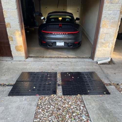 Close-up of a low sports car using modular rubber ramps to climb over a raised garage threshold without scraping.