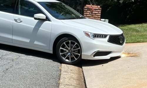 Low-clearance car front bumper scraping on a steep driveway lip during angled entry
