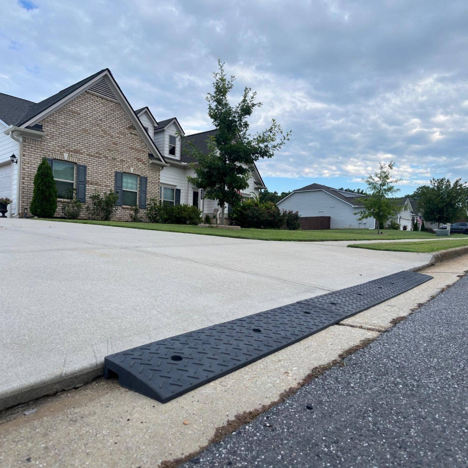 Rubber driveway curb lip ramp installed at the street edge to reduce the sharp curb drop-off that causes low cars to scrape when entering the driveway.