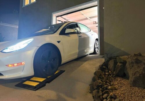 Wide view of a low-profile car driving out of a garage over a rubber curb ramp to smooth a steep driveway transition and avoid bottoming out.