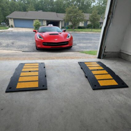Sports car approaching a garage with rubber garage entry ramps positioned to prevent scraping on a steep driveway transition.